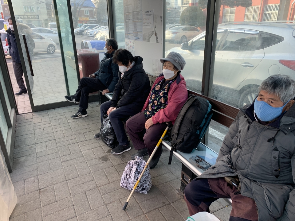 버스승강장의 온열의자에 앉아 버스를 기다리는 시민들.