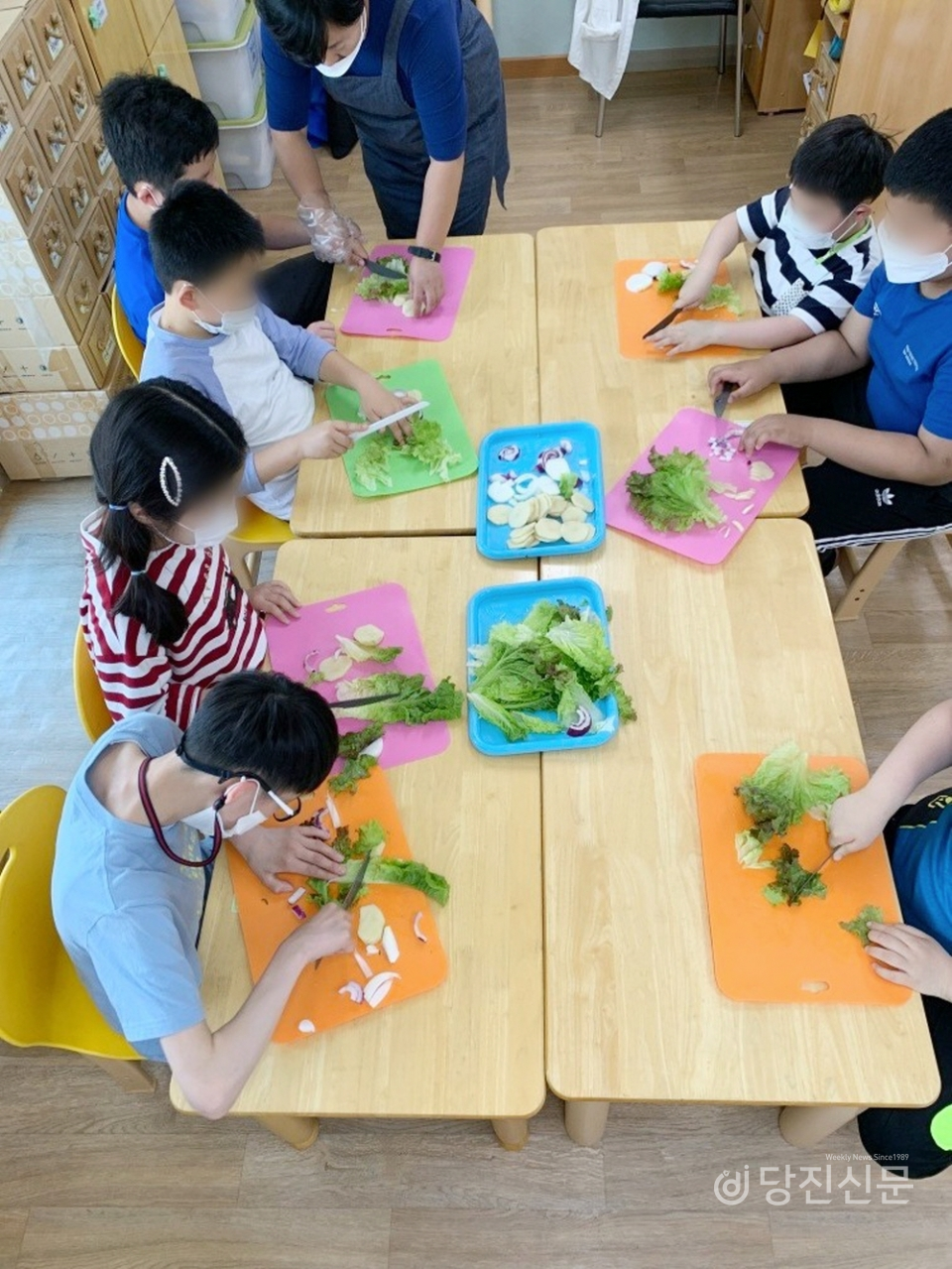 아이들이 선생님의 도움을 받으며 채소를 자르려 노력하는 모습.